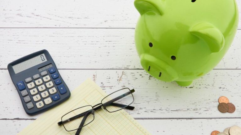 Tirelire verte, calculatrice, lunettes et pièces sur une table