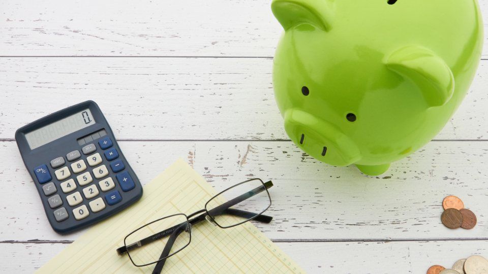Tirelire verte, calculatrice, lunettes et pièces sur une table